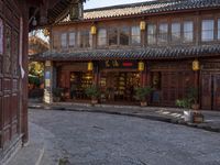 a street outside a large stone building with wooden doors and windows decorated with asian lanterns