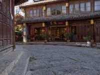 a street outside a large stone building with wooden doors and windows decorated with asian lanterns