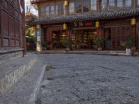 a street outside a large stone building with wooden doors and windows decorated with asian lanterns