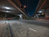 a city street at night with light traffic underneath the bridge and some lights hanging over it