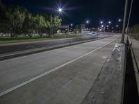 an empty road with some lights over it at night near a tree lined street and a grass field