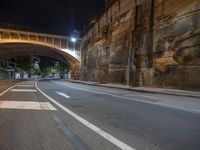 street at night with a roadway leading under a bridge in the middle of town, with the lights on