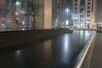 an empty bench outside of the building next to a sidewalk on a city street in the evening