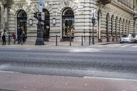 the corner of a street with people walking on it, and a car in the background