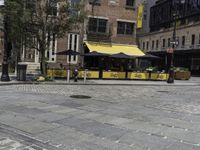 a restaurant with a yellow awning sitting in the middle of a city street area