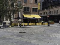 a restaurant with a yellow awning sitting in the middle of a city street area