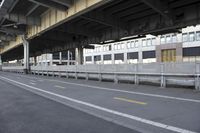 a train sits on the tracks under an overpass on a street area with buildings
