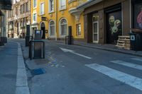 a paved city street with buildings on the sides and a painted crosswalk and bench near the curb