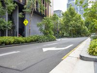 a street in a city with buildings and trees on either side and green bushes along the street