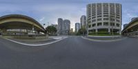 a fisheye lens photograph of a city street with tall buildings in the background and a person riding a skateboard on the road at the corner