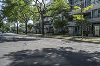 a city street with several tall trees and green lawns with parked cars on one side and two on the other