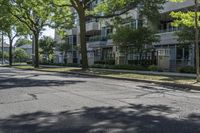 a city street with several tall trees and green lawns with parked cars on one side and two on the other