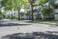 a city street with several tall trees and green lawns with parked cars on one side and two on the other