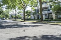 a city street with several tall trees and green lawns with parked cars on one side and two on the other