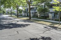 a city street with several tall trees and green lawns with parked cars on one side and two on the other