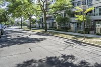 a city street with several tall trees and green lawns with parked cars on one side and two on the other