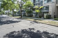 a city street with several tall trees and green lawns with parked cars on one side and two on the other