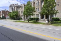 a city street lined with older brick apartment buildings near green shrubs and fenced green lawns