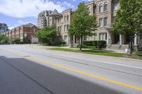 a city street lined with older brick apartment buildings near green shrubs and fenced green lawns