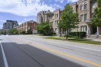 a city street lined with older brick apartment buildings near green shrubs and fenced green lawns