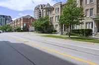 a city street lined with older brick apartment buildings near green shrubs and fenced green lawns