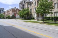 a city street lined with older brick apartment buildings near green shrubs and fenced green lawns