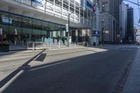 a city street with a traffic light and tall buildings in the background with a fence on one side and some bushes growing outside