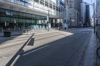 a city street with a traffic light and tall buildings in the background with a fence on one side and some bushes growing outside