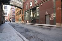 an alley way with people walking along and two cars in the street and buildings behind