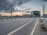 city streets with empty highway and a modern looking building on horizon behind them by cloudy sky