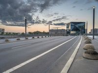 city streets with empty highway and a modern looking building on horizon behind them by cloudy sky