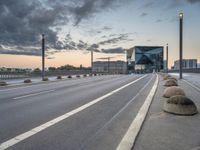 city streets with empty highway and a modern looking building on horizon behind them by cloudy sky