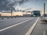 city streets with empty highway and a modern looking building on horizon behind them by cloudy sky