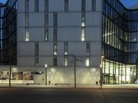 a paved street in the middle of buildings with tall windows at night, with car lights on