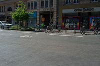 four bikes are on the street near a row of stores and cars and parked cars