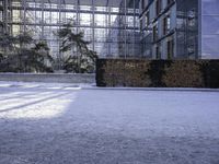 a snow covered area with bushes and shrubs next to glass buildings and glass walkways