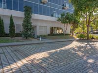 an apartment building with some glass windows and trees in the courtyard area of it to the sidewalk