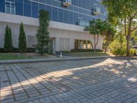 an apartment building with some glass windows and trees in the courtyard area of it to the sidewalk