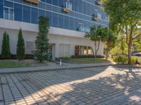 an apartment building with some glass windows and trees in the courtyard area of it to the sidewalk