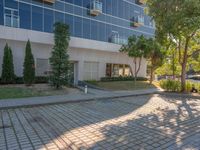 an apartment building with some glass windows and trees in the courtyard area of it to the sidewalk