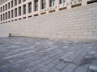 a person walking in the foreground on a stone pavement outside of a building, with a sign that reads umbold forum