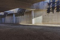large concrete building with multiple vertical beams on it's walls, and another floor area to the left that has multiple small openings