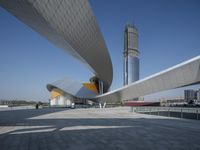 a person walks near an architectural structure on the edge of a road surrounded by large buildings