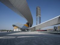 a person walks near an architectural structure on the edge of a road surrounded by large buildings