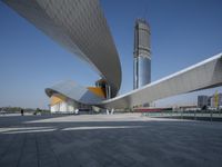 a person walks near an architectural structure on the edge of a road surrounded by large buildings