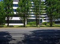 a white building with lots of windows next to trees and bushes on the side of the road