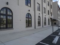 the empty parking lot is next to the white brick building with many windows in front and around the car