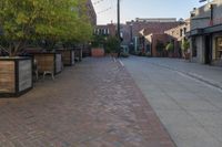 an empty brick sidewalk in front of a red brick building with several chairs, benches and tables on the side