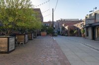 an empty brick sidewalk in front of a red brick building with several chairs, benches and tables on the side