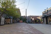 an empty brick sidewalk in front of a red brick building with several chairs, benches and tables on the side